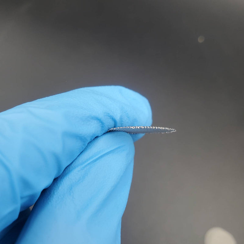 A close-up view of a round stainless steel pipe screen held by a gloved hand, showing the fine mesh details.