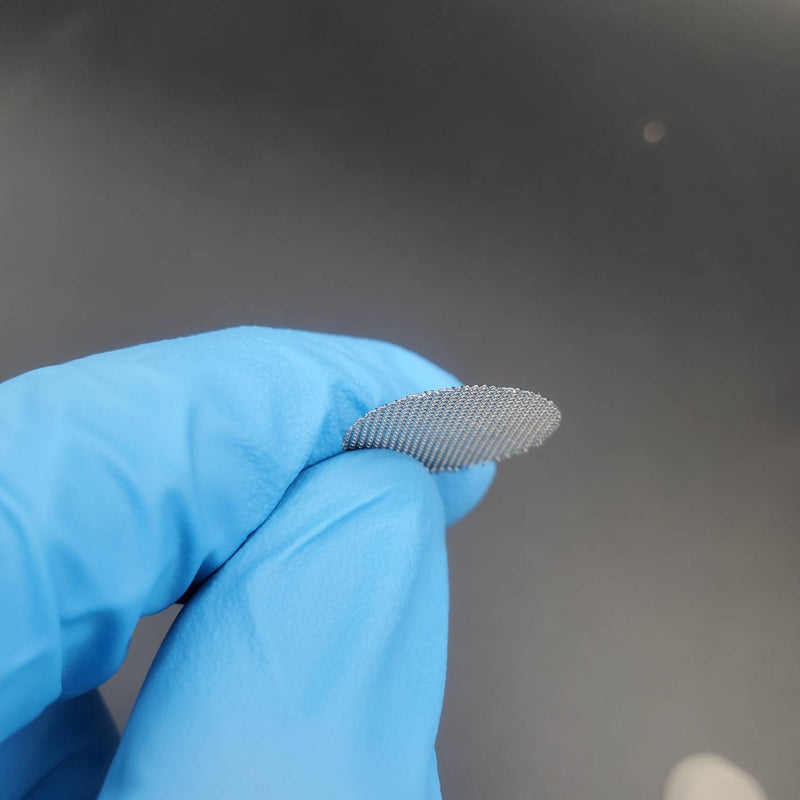  A round stainless steel screen held by a gloved hand, designed for use in smoking pipes.